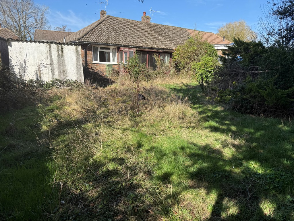 Lot: 128 - BUNGALOW WITH GARAGE AND GARDENS IN NEED OF MODERNISATION - Overgrown rear garden with trees and shrubs